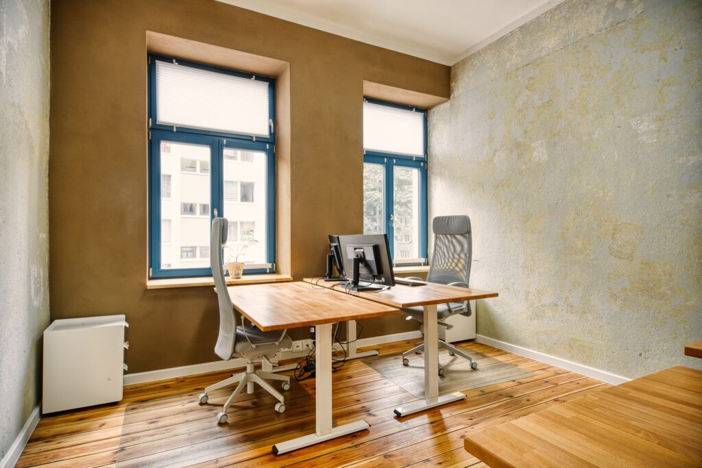 Zwei höhenverstellbare Schreibtische mit bequemen Bürostühlen vor großen Fenstern - das sind die Fixdesks im Coworking Magdeburg.